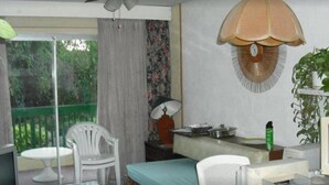 A room with a bed, a desk, a chair, a ceiling fan, a hanging lamp, and a view of greenery outside. - Walmer Lodge Apartments (Bridgetown)