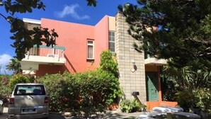 A building with a red facade, a balcony, and a small garden area with a fountain. - Walmer Lodge Apartments (Bridgetown)