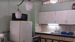 A compact kitchen with white cabinets, a microwave, a stove, and a sink. - Walmer Lodge Apartments (Bridgetown)
