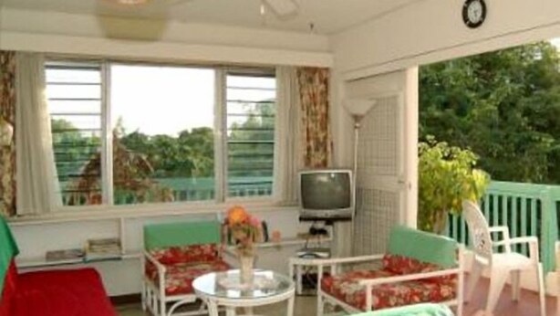 A room with a ceiling fan, a television, a table with a vase, and two chairs. - Walmer Lodge Apartments (Bridgetown)