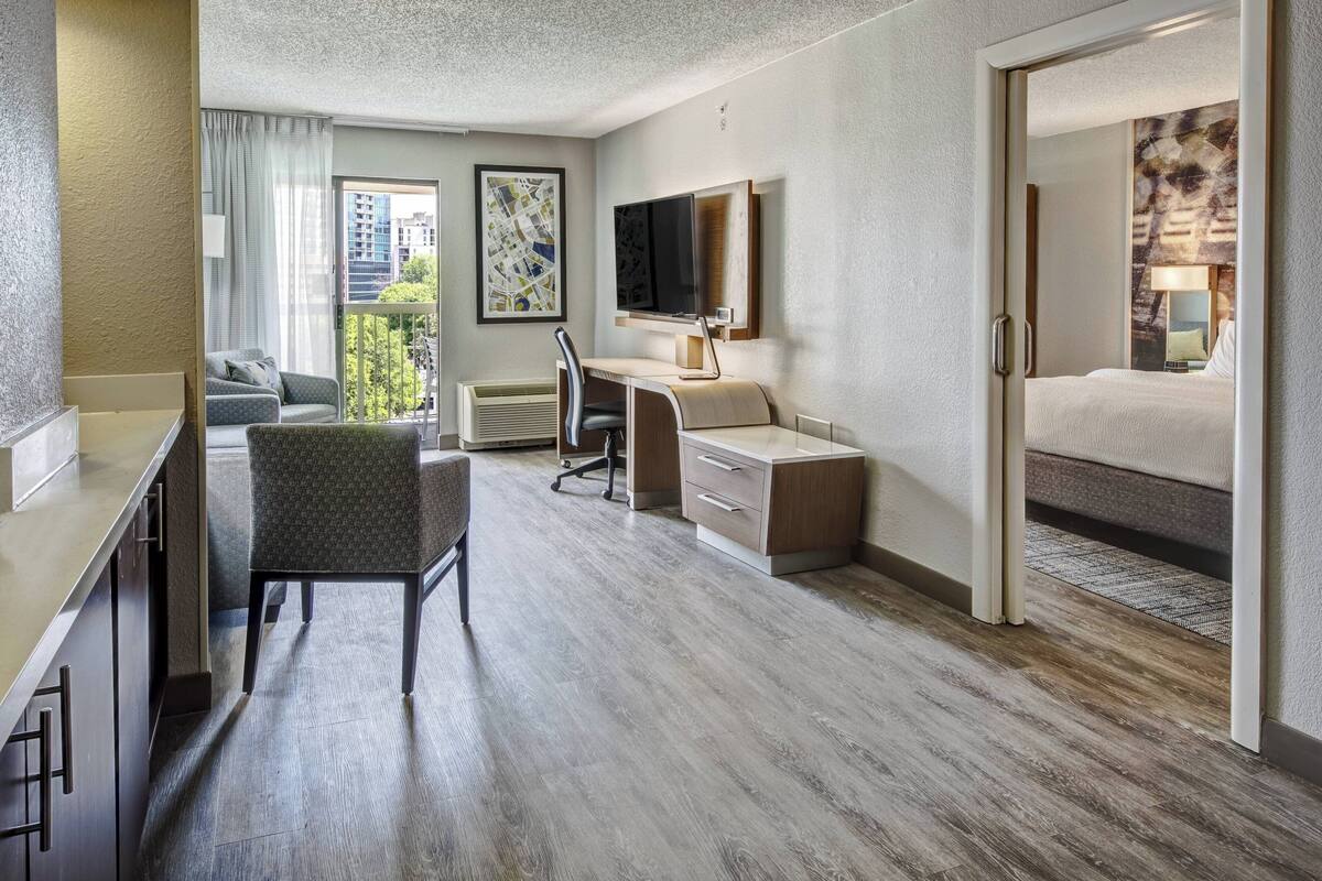A hotel room with a bed, desk, chair, and a view of the cityscape.