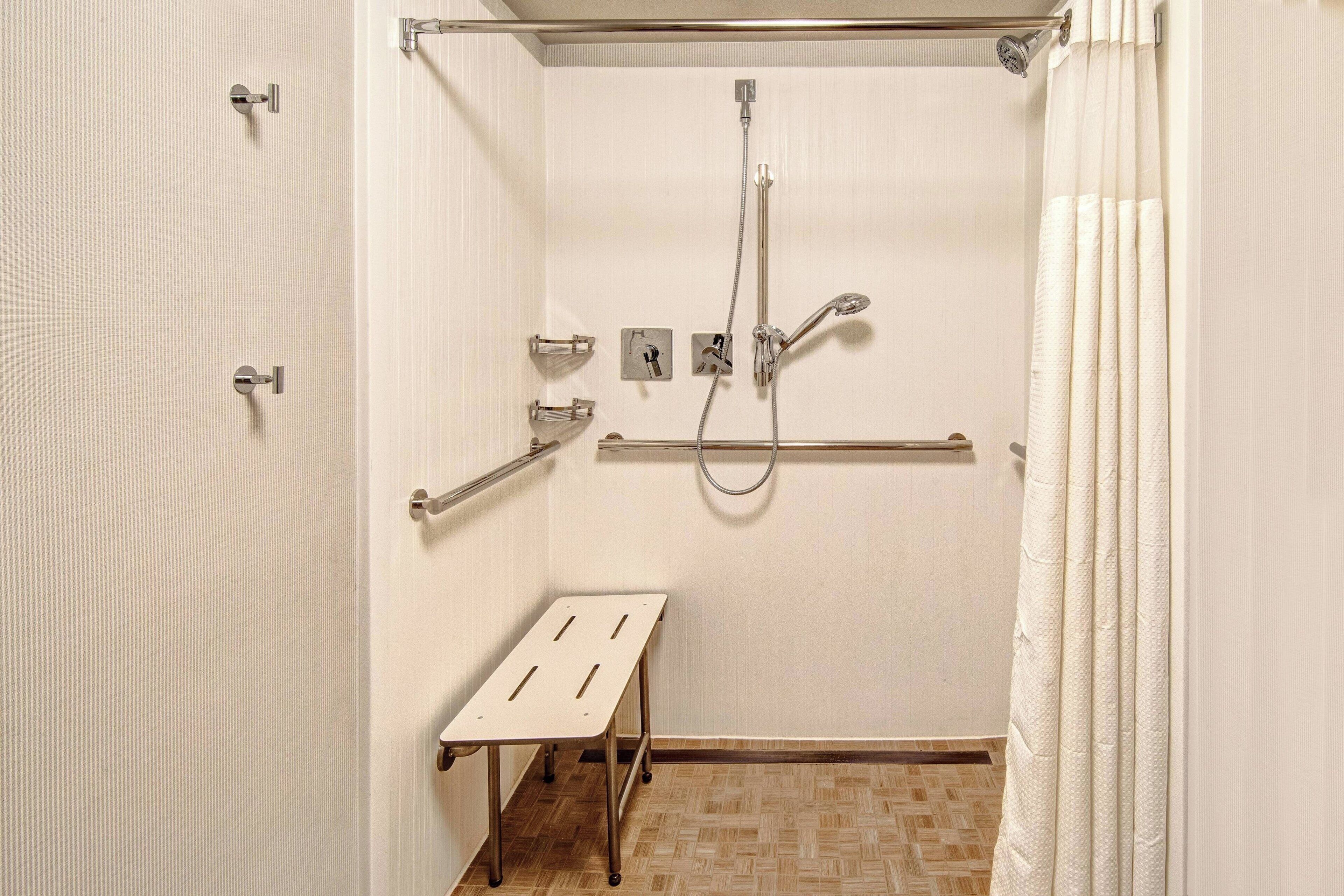 A bathroom with a shower, grab bars, a bench, and a towel rack.
