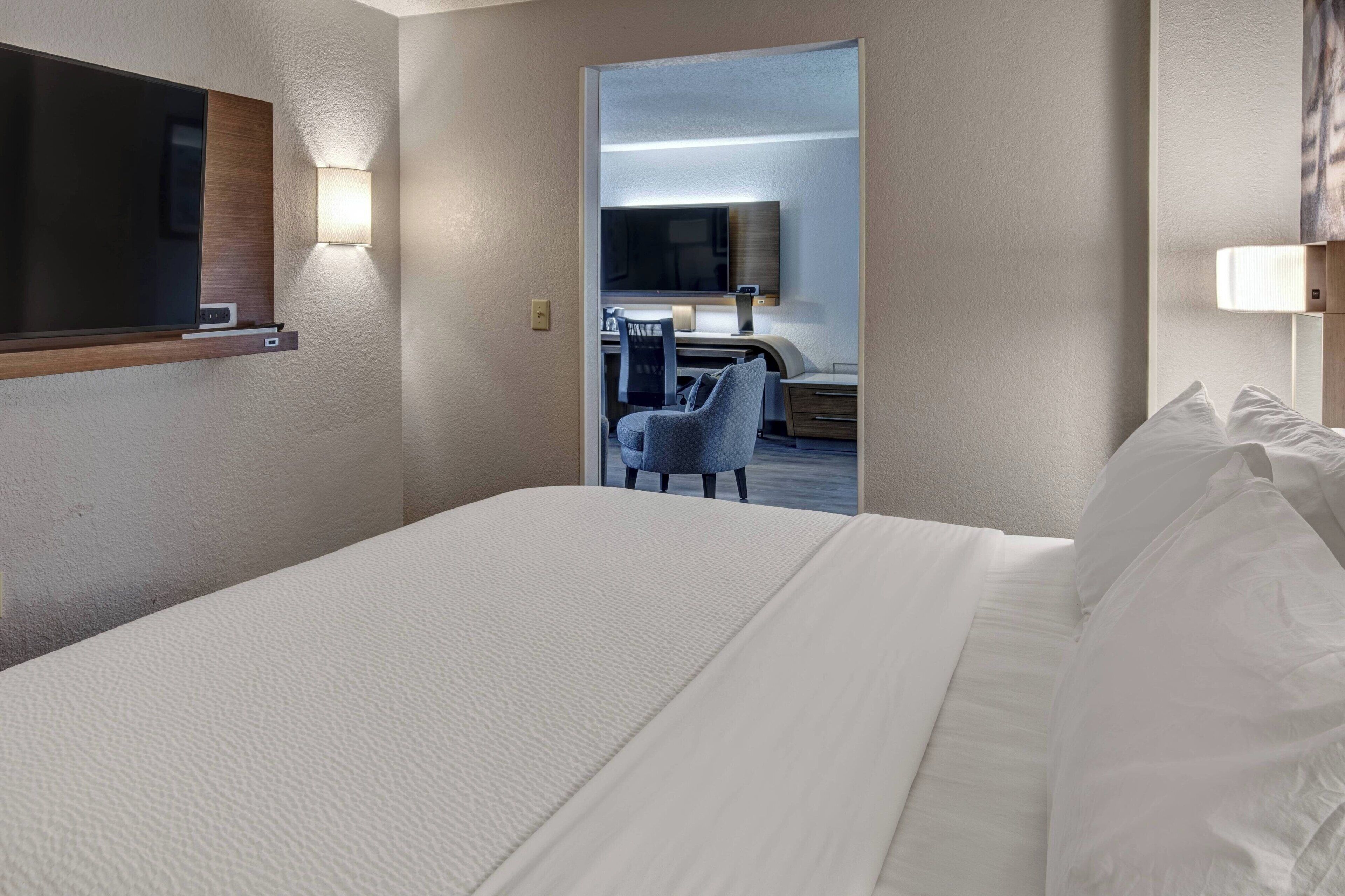 Une chambre d’hôtel avec un grand lit, un bureau avec une chaise, un téléviseur à écran plat et une lampe fixée au mur.