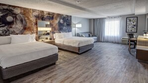 Una camera d'albergo con due letti, una scrivania, una sedia, un quadro astratto di grandi dimensioni e una finestra con tende.