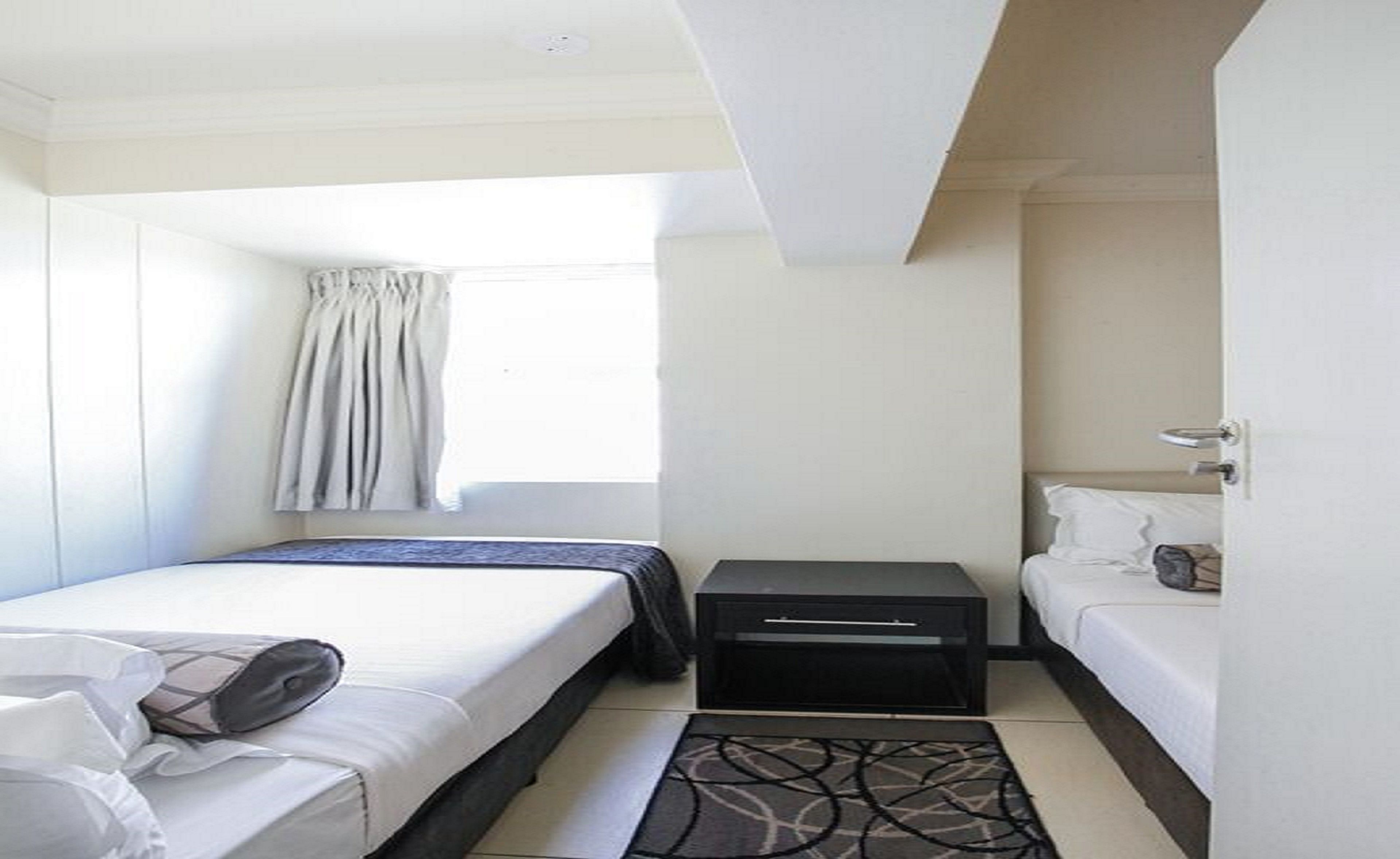 Una habitación de hotel pequeña y bien iluminada con una cama individual, una mesita de noche, un escritorio pequeño y una ventana con cortinas.