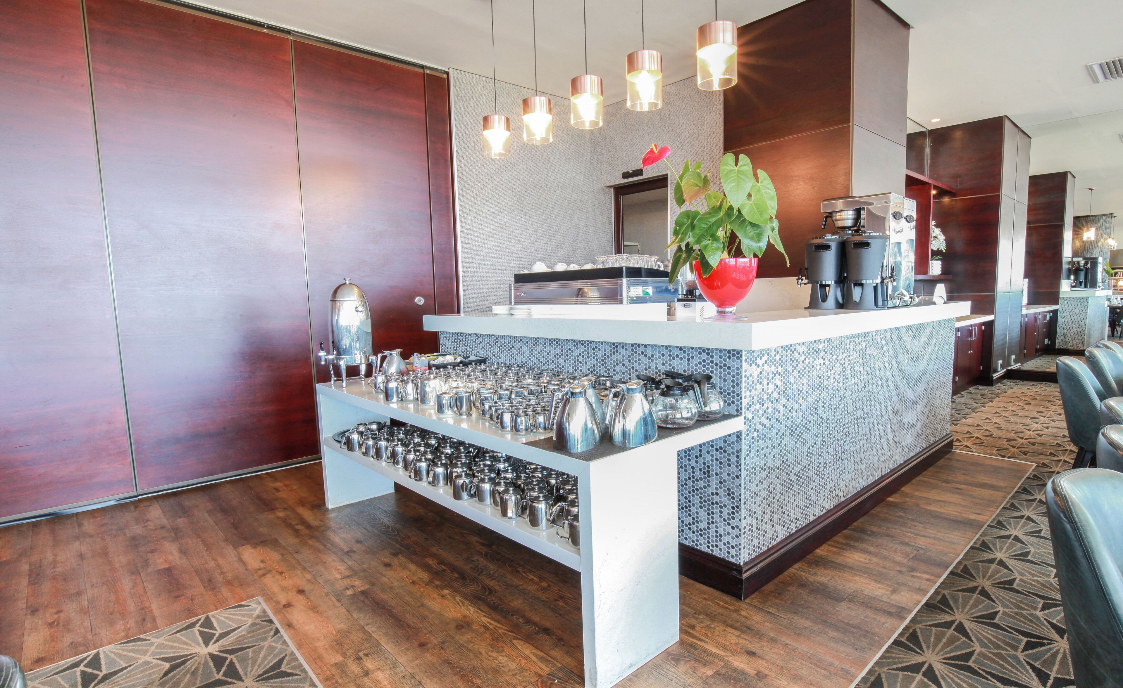 A modern kitchen area with a coffee station, stainless steel appliances, and a decorative plant.