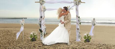 A beach wedding ceremony with a white arch and floral decorations.