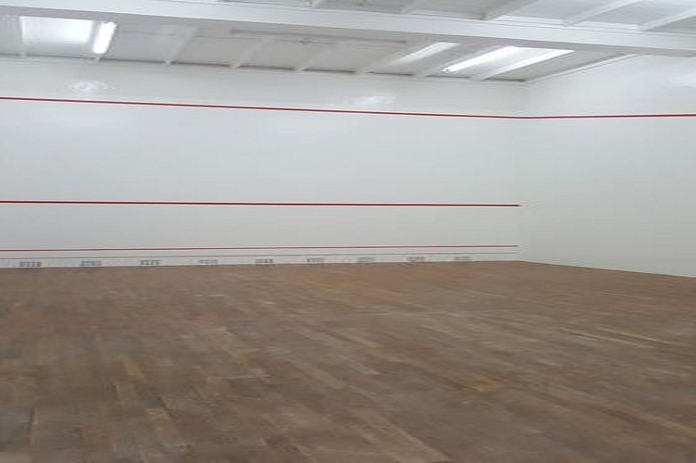 A spacious indoor area with a wooden floor and white walls marked with red lines.
