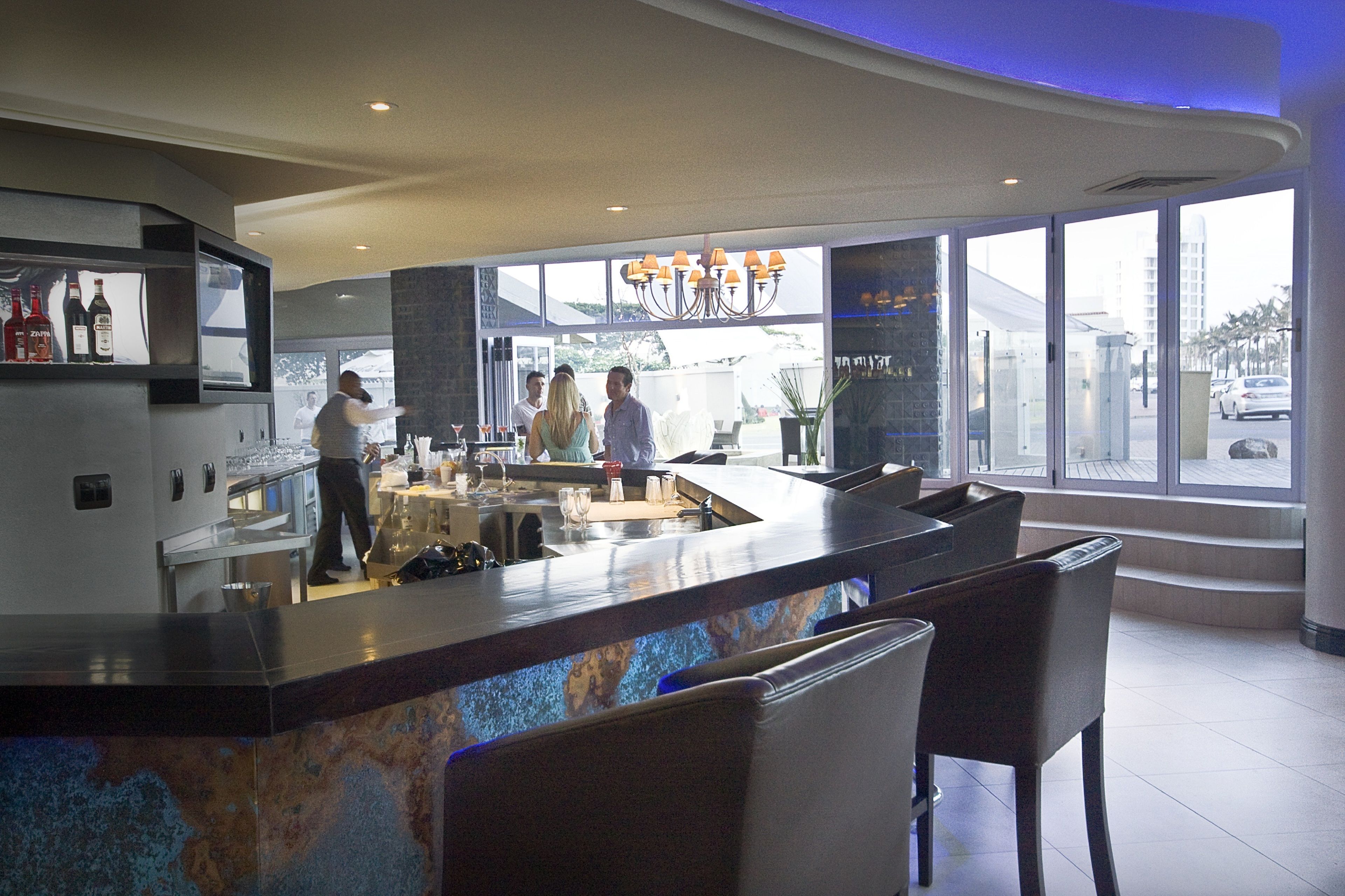 Un área de bar moderna con mostrador de mármol, taburetes y vistas de la ciudad a través de amplias ventanas.