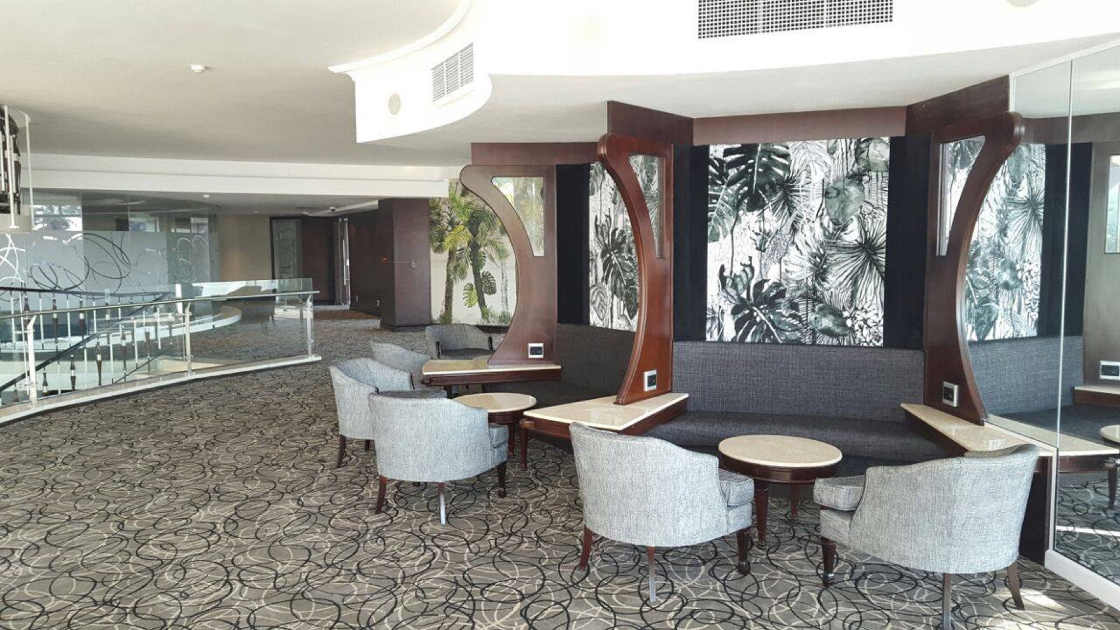 A modern lobby with a patterned carpet, seating areas, and large windows with tropical artwork.