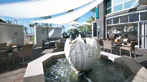 A patio area with outdoor seating, a decorative water feature, and a building with large windows. - The Blue Waters Hotel (Durban)