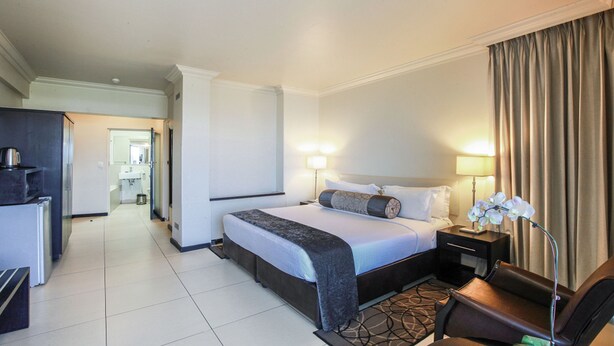 A hotel room with a bed, bedside tables, a desk, and a lamp. - The Blue Waters Hotel (Durban)