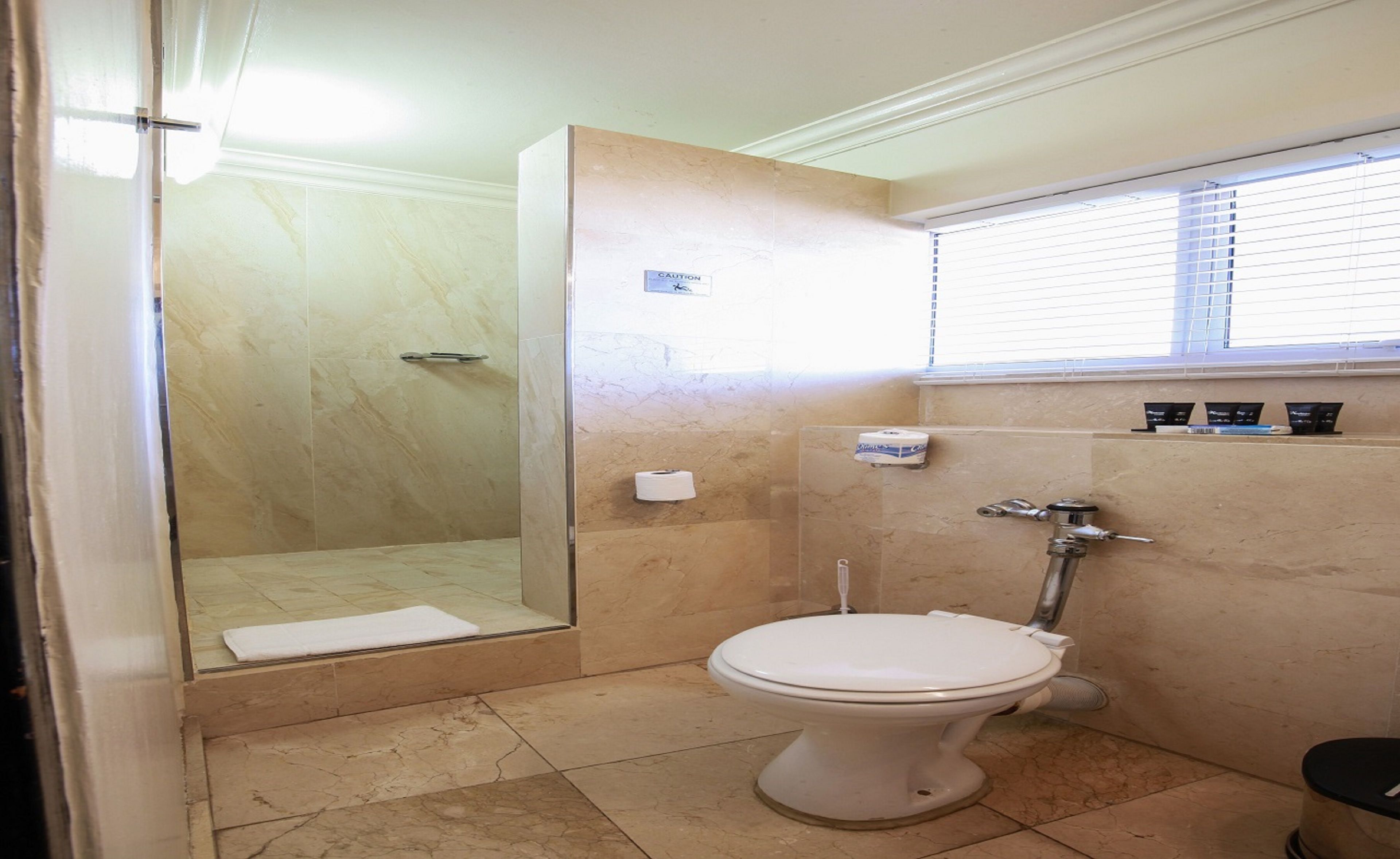Une salle de bain avec douche, toilettes et une fenêtre équipée de stores.