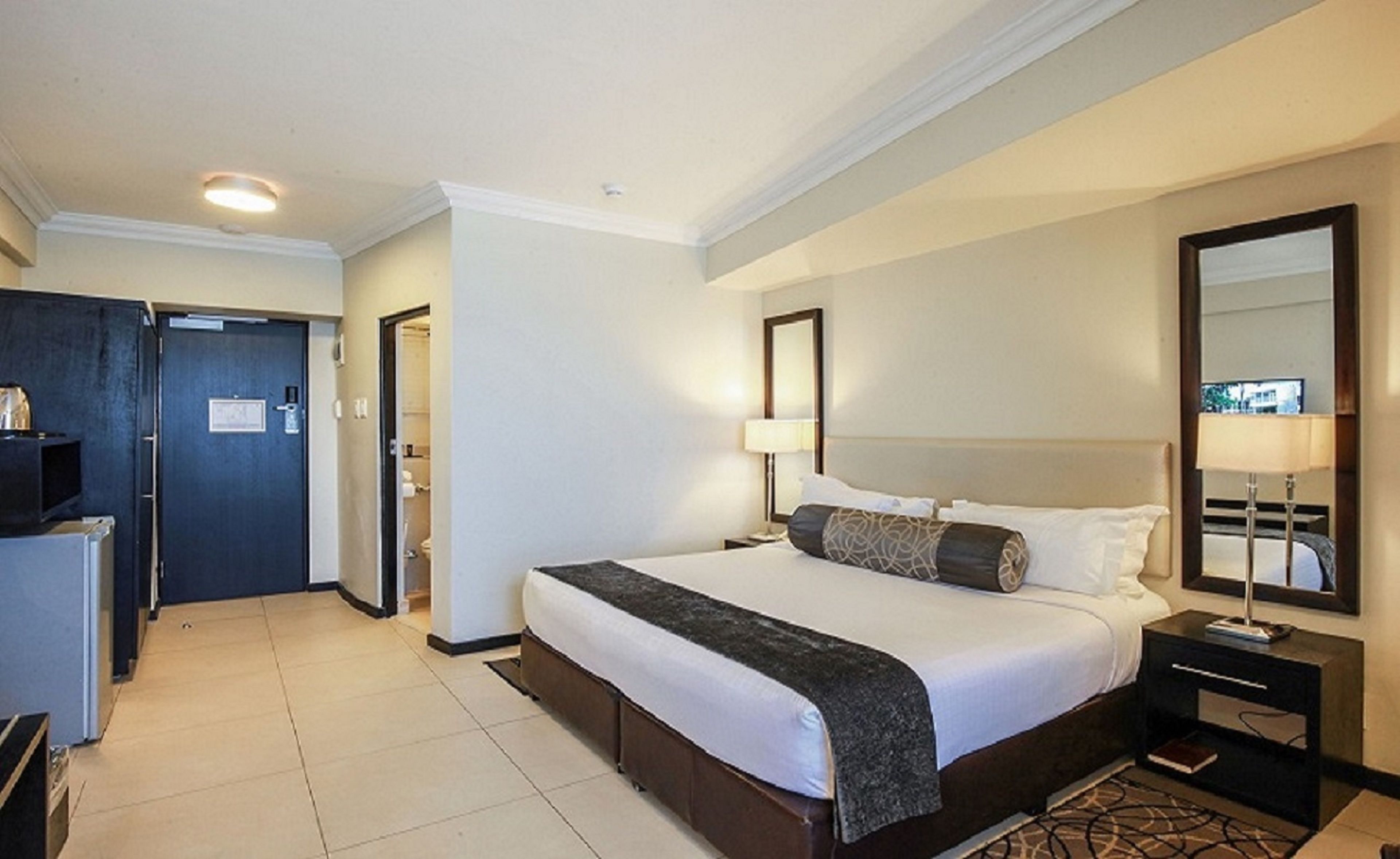 Une chambre d’hôtel avec un grand lit, une table de chevet, un miroir et une porte donnant sur une salle de bain.