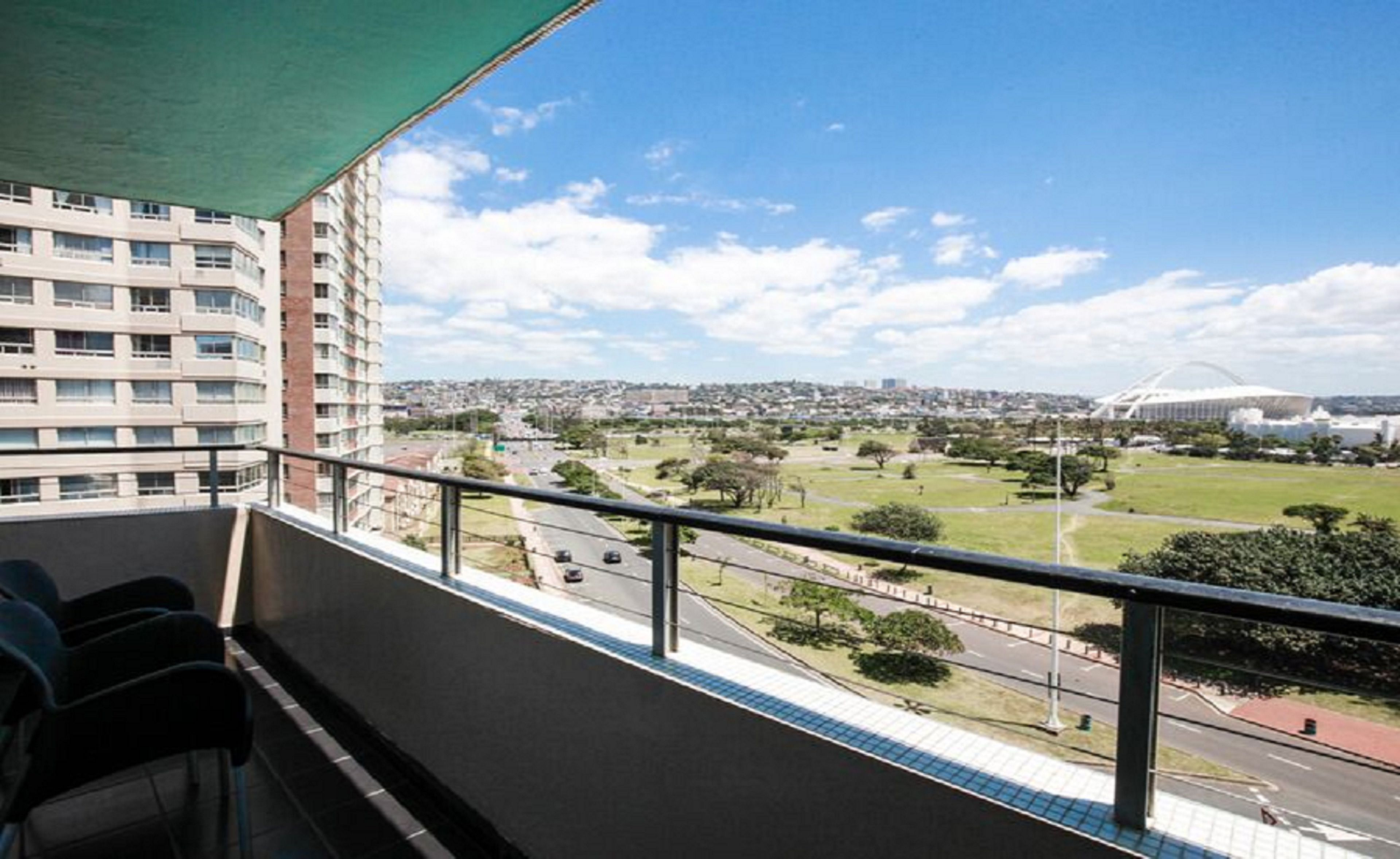 Un balcon offrant une vue sur le paysage urbain, notamment un stade et des immeubles d’habitation.