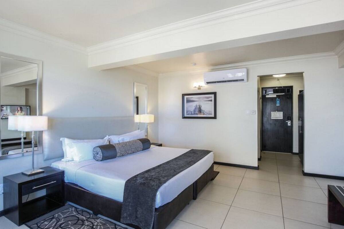 A hotel room with a bed, bedside table, lamp, and a picture on the wall.