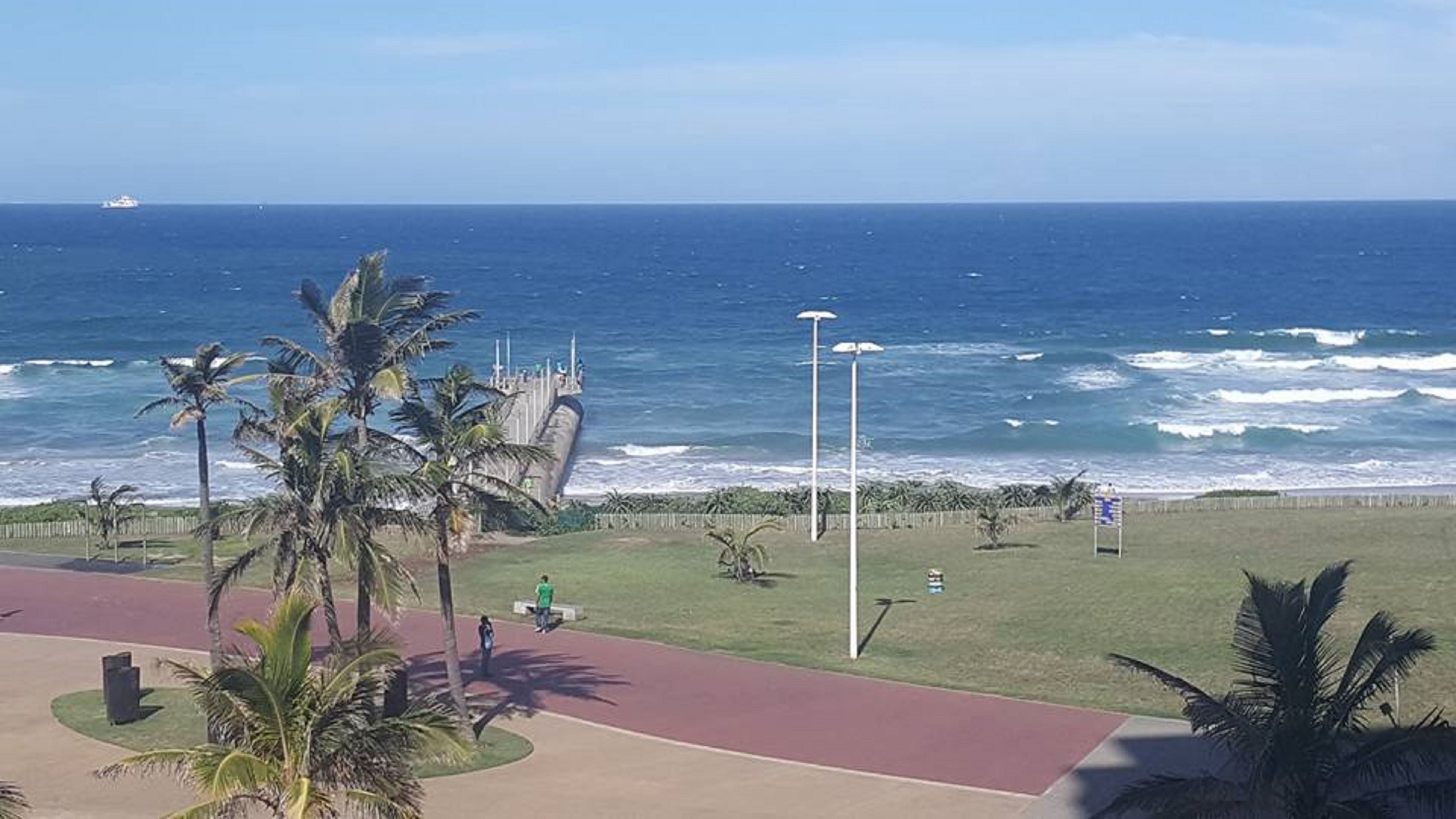 A coastal view with a paved walkway, palm trees, and a view of the ocean.