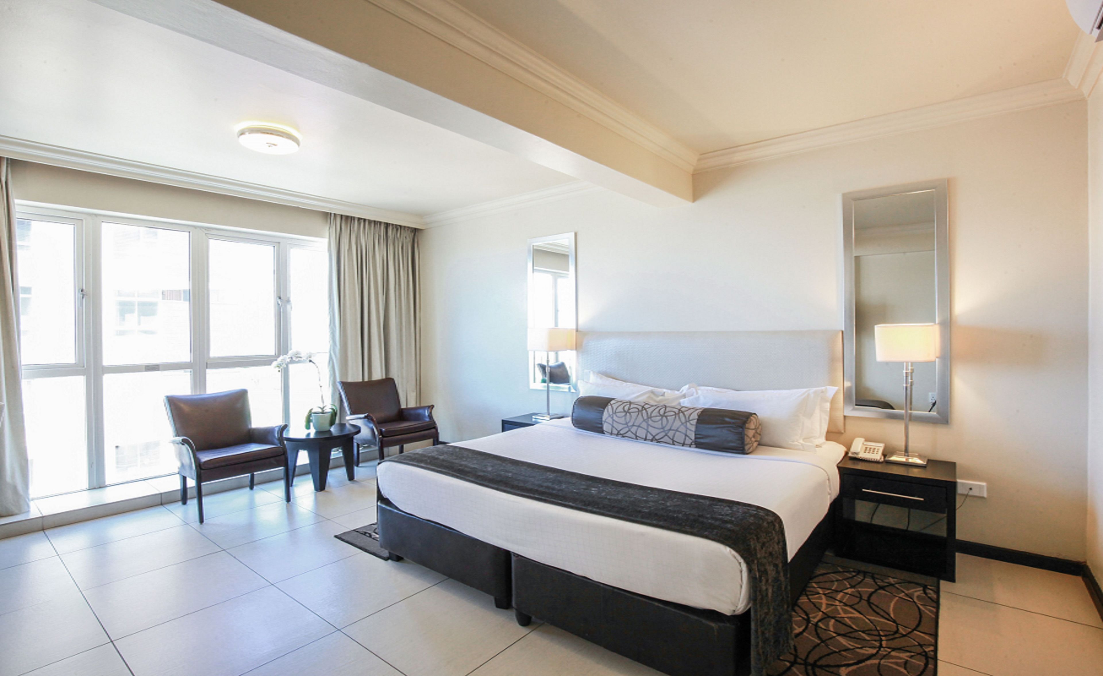 A hotel room with a large bed, a chair, a desk, and a window with curtains.