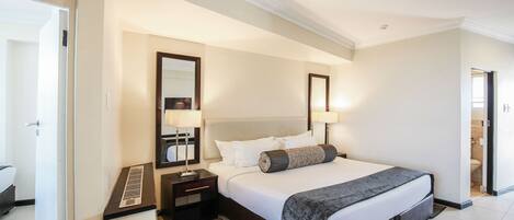 A hotel room with a large bed, two bedside tables, a mirror, and a view of the bathroom.
