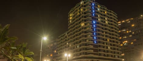 Un hotel de varios pisos con fachada curva, señalización iluminada y una entrada bien iluminada.