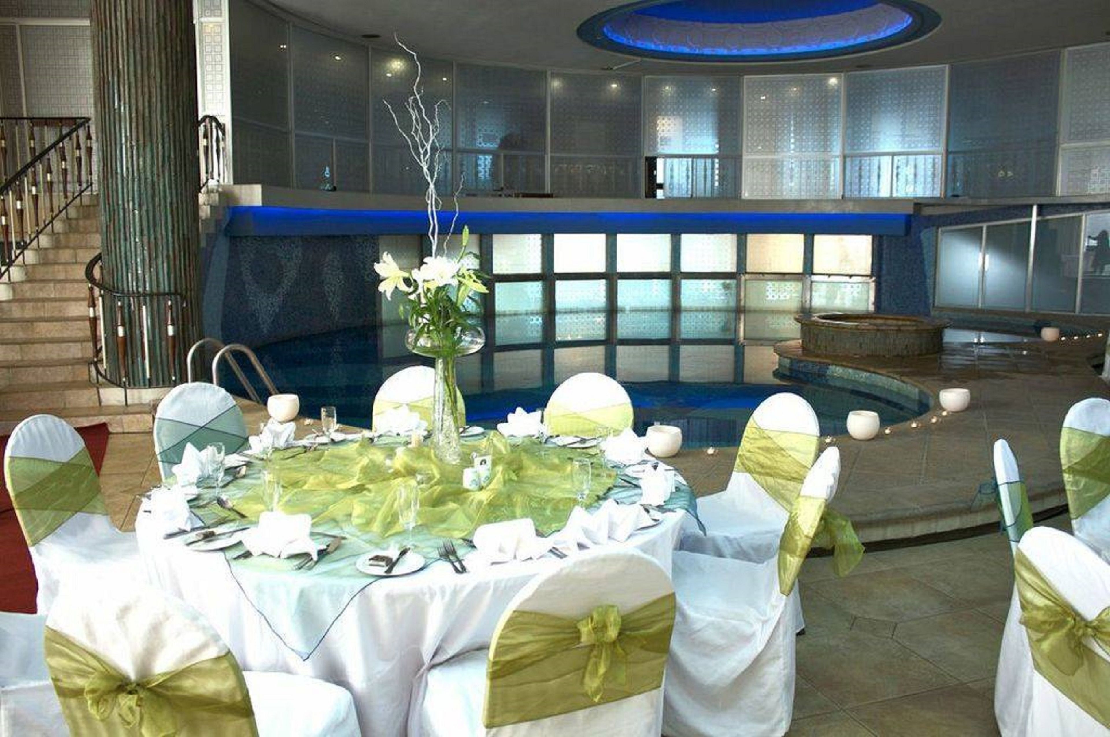 Montaje formal para comedor con mesas redondas, manteles blancos y sillas con cintas verdes.