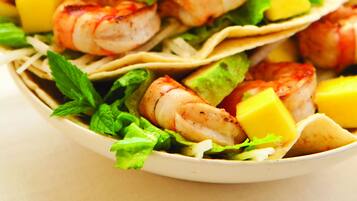 Een schaal garnalen taco's met avocado en mango, geserveerd op een wit bord.