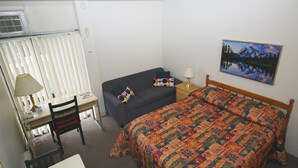 A bedroom with a bed, a desk, a chair, a sofa, a lamp, and a painting on the wall.