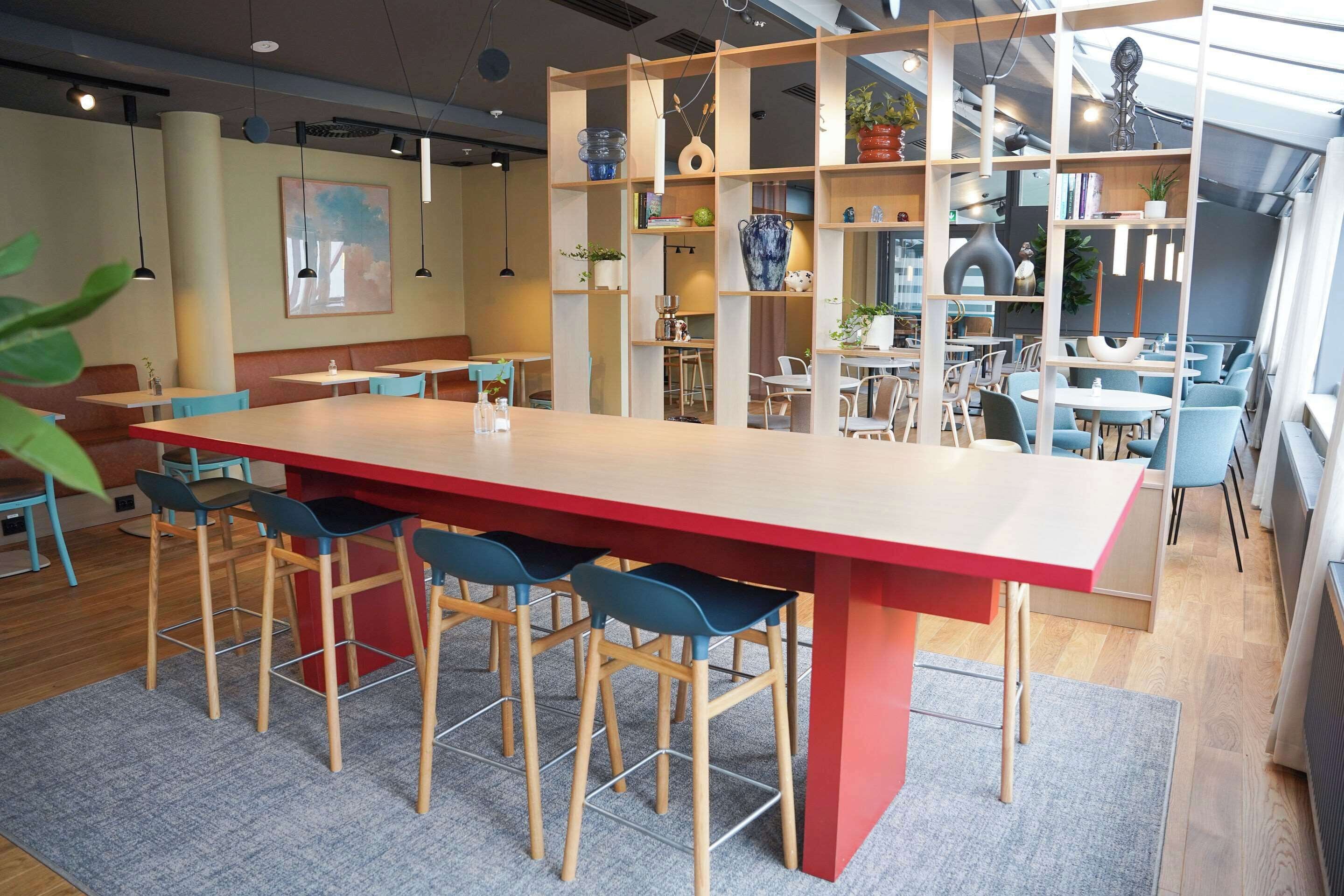 A modern dining area with a long red table, blue chairs, and a wooden floor.