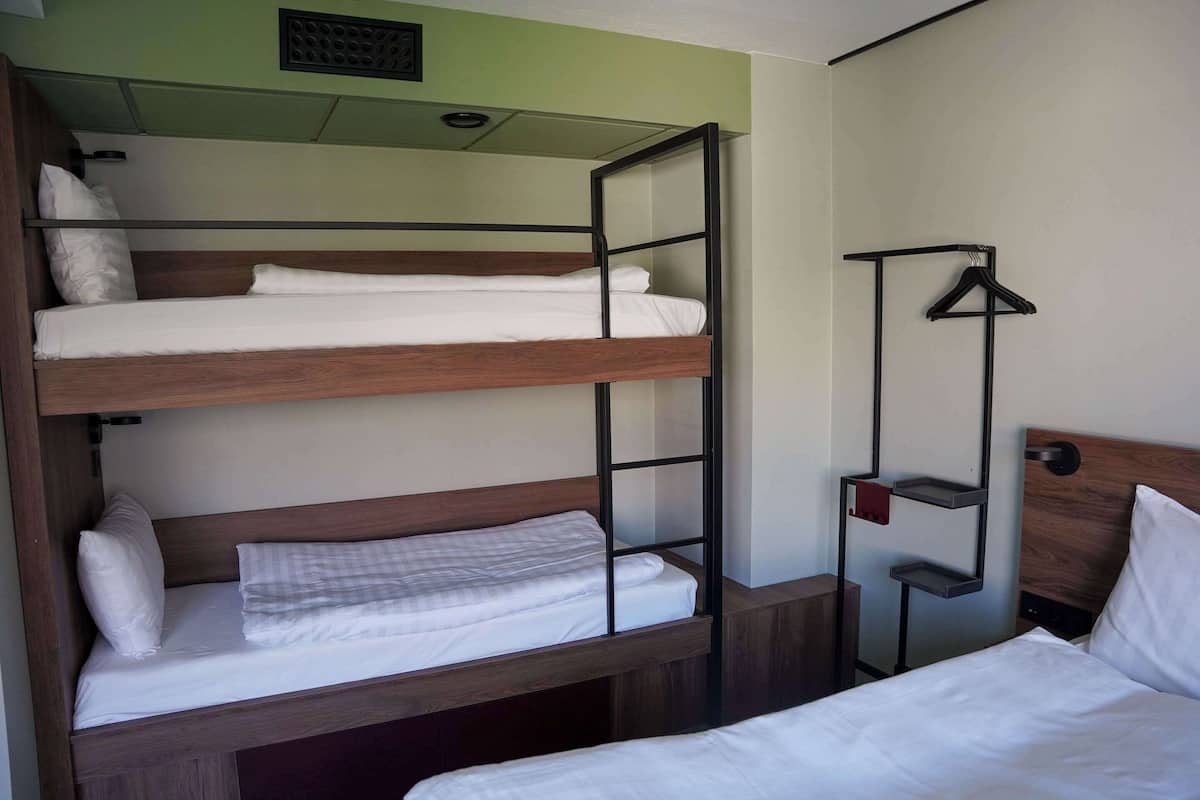 Quarto com beliche, cabeceira de madeira, cabideiro e prateleira pequena.