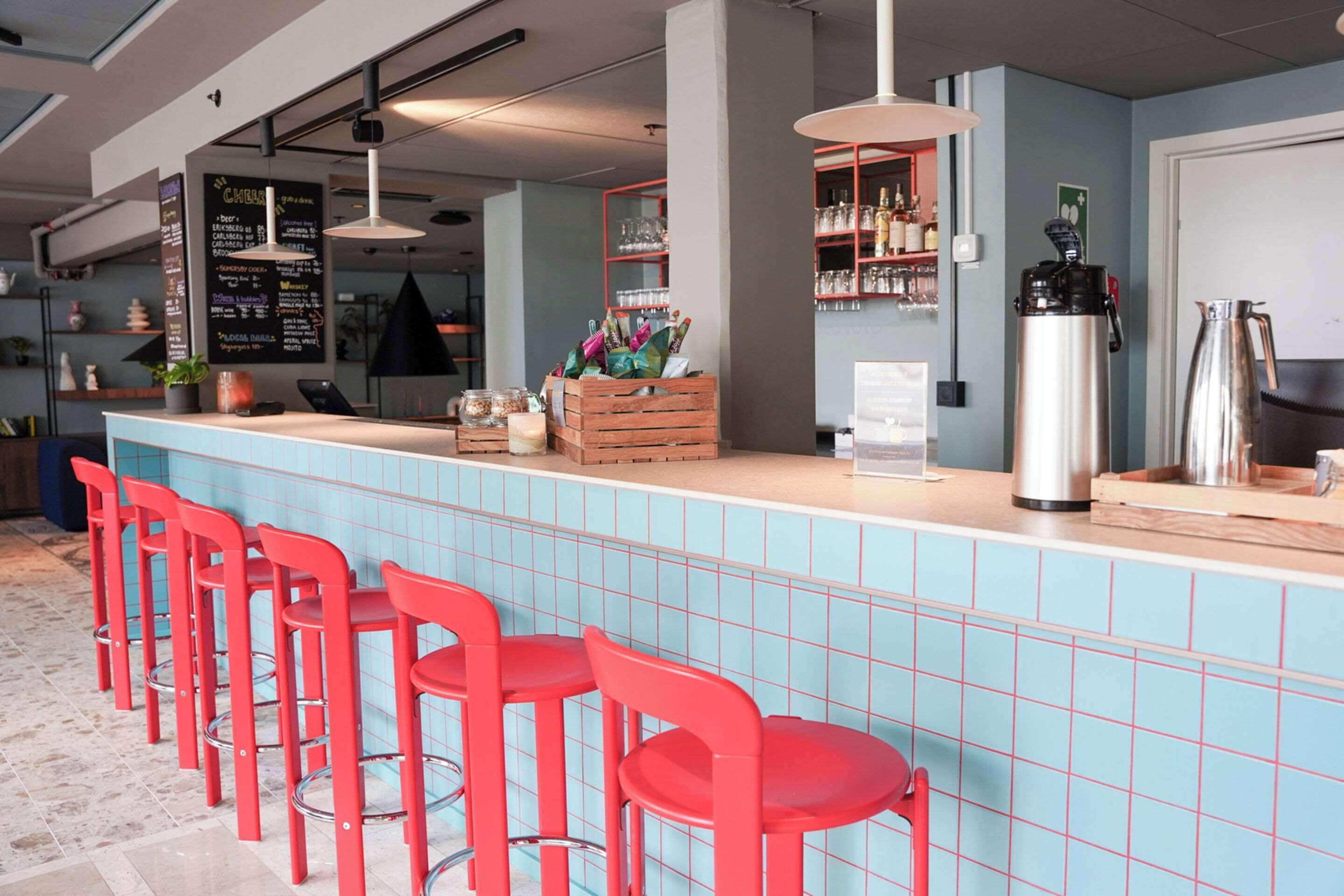 Un espace bar avec des tabourets rouges, un comptoir recouvert de carreaux bleus et un tableau affichant le menu.