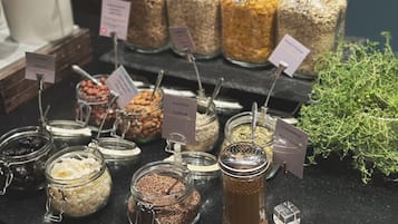 Variedad de alimentos en frascos de vidrio etiquetados, como frutos secos, semillas y cereales, expuestos sobre una encimera.