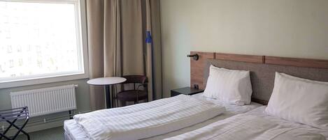 A hotel room with two beds, a window with curtains, a small table, and a chair.