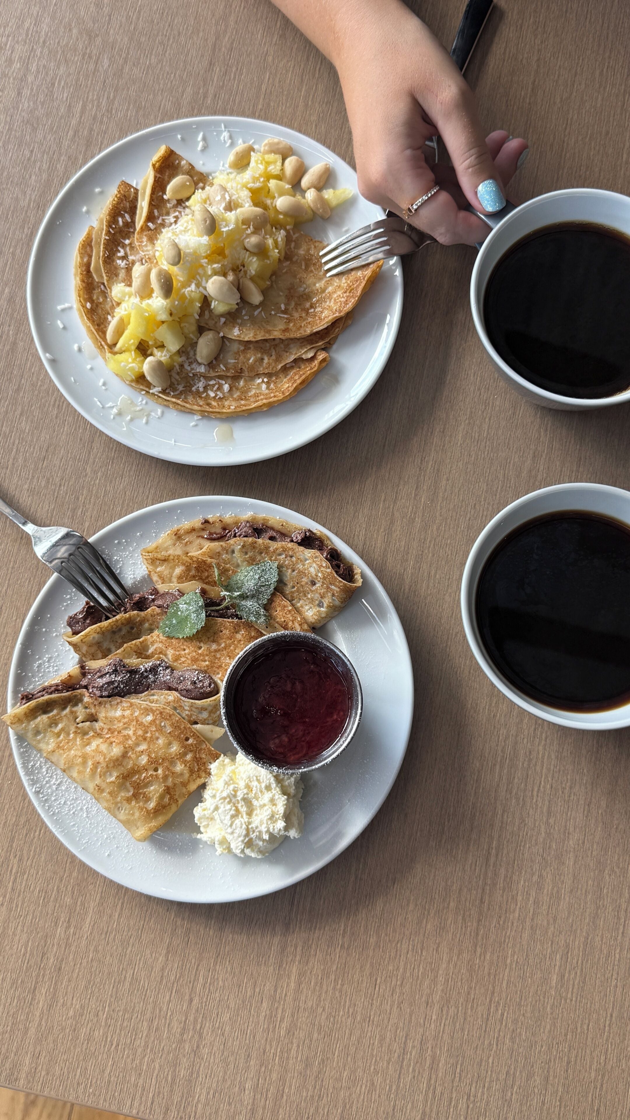 Una mesa con dos platos de comida, una taza de café y una mano sosteniendo un tenedor.