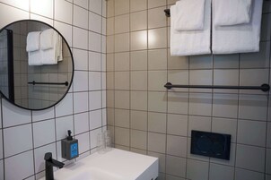 Un baño con un espejo redondo, un lavamanos blanco, un toallero con toallas dobladas, una barra para toallas y un dispensador de jabón.