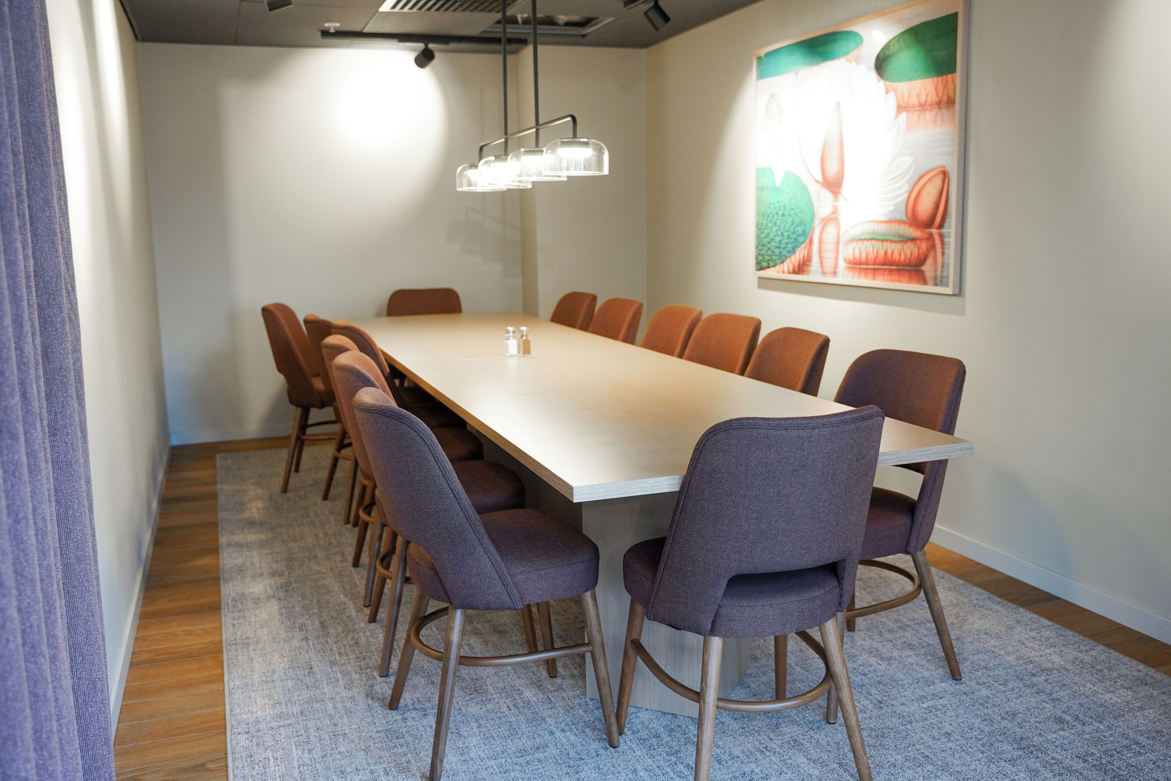 Un salón de conferencias con una mesa larga, varias sillas, una lámpara en el techo y un cuadro en la pared.