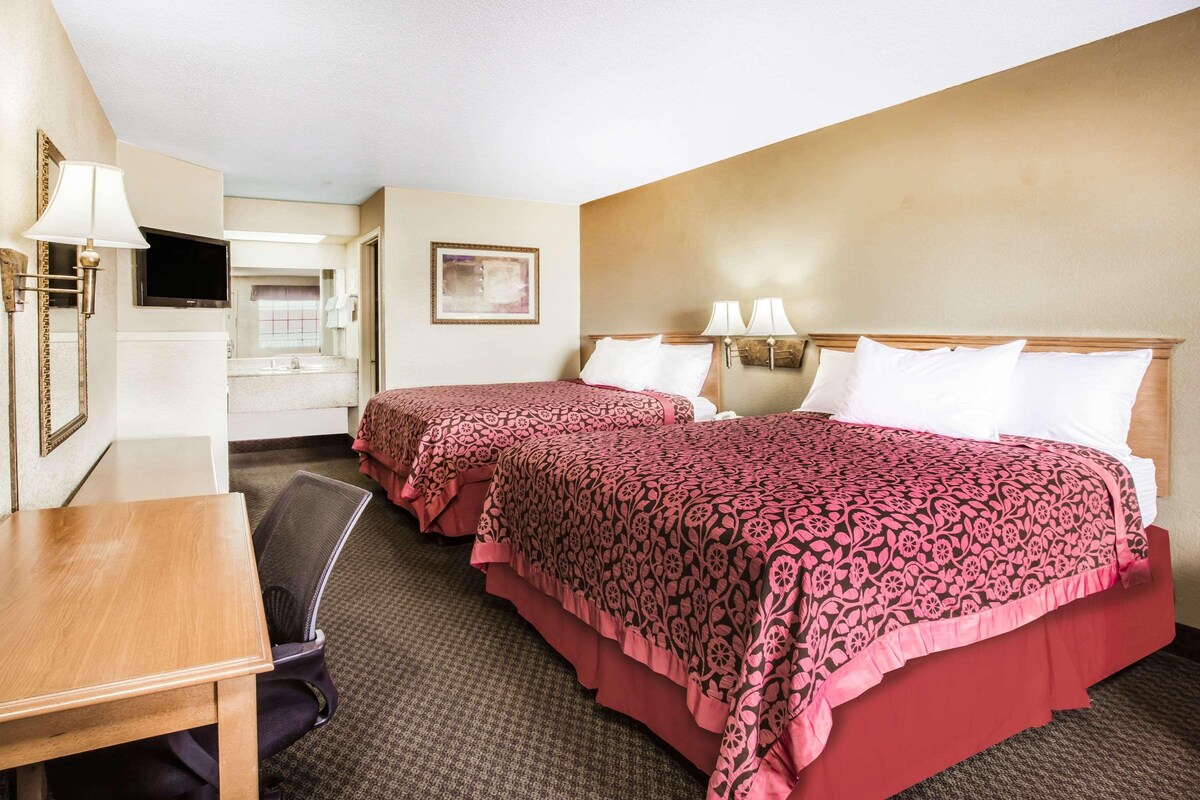 Une chambre d’hôtel avec deux lits, un bureau, une chaise, une télévision et une salle de bain visible à travers une porte ouverte.