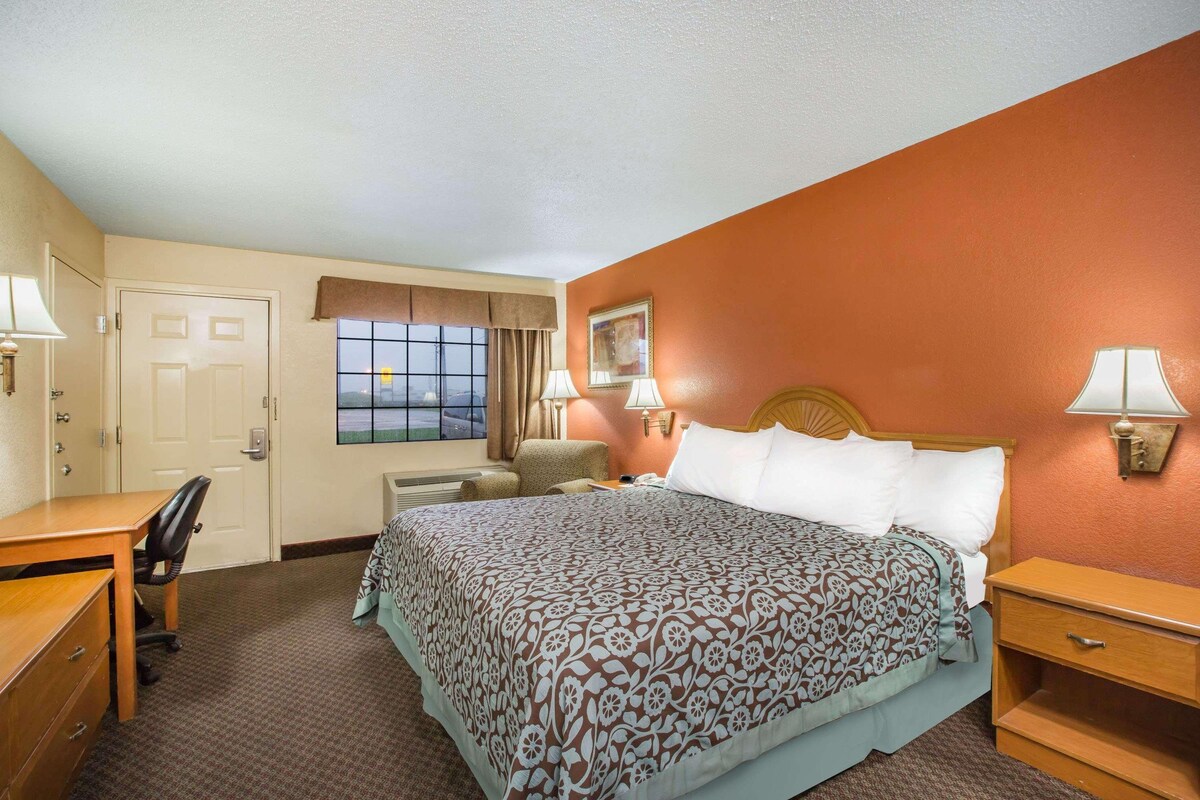 Une chambre d’hôtel comprenant un lit, des tables de chevet, un bureau, une chaise, une fenêtre avec des rideaux et une vue sur l’extérieur.