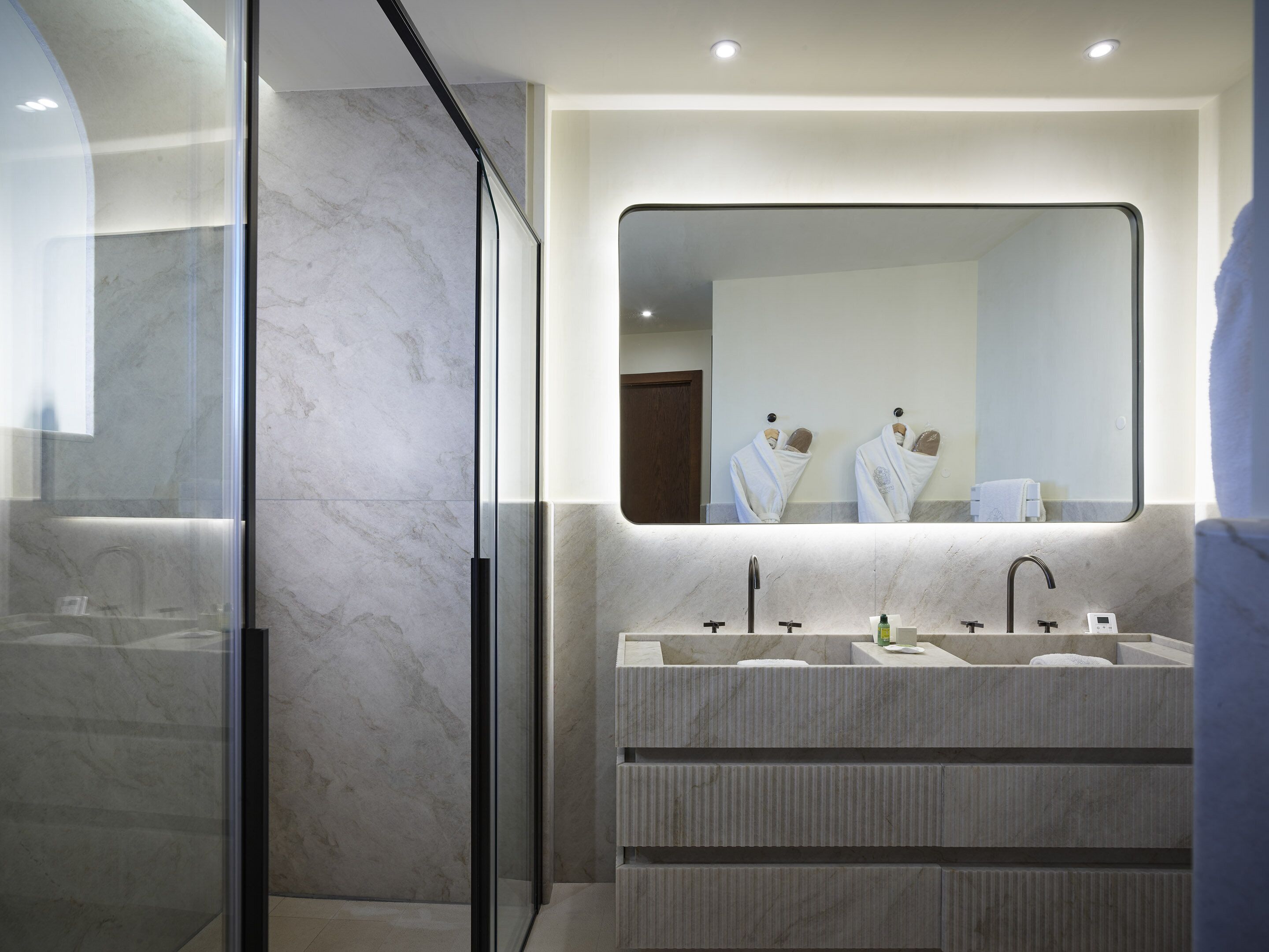 Un baño moderno con cabina de ducha de vidrio, un espejo grande y un lavamanos triple con encimera de mármol.