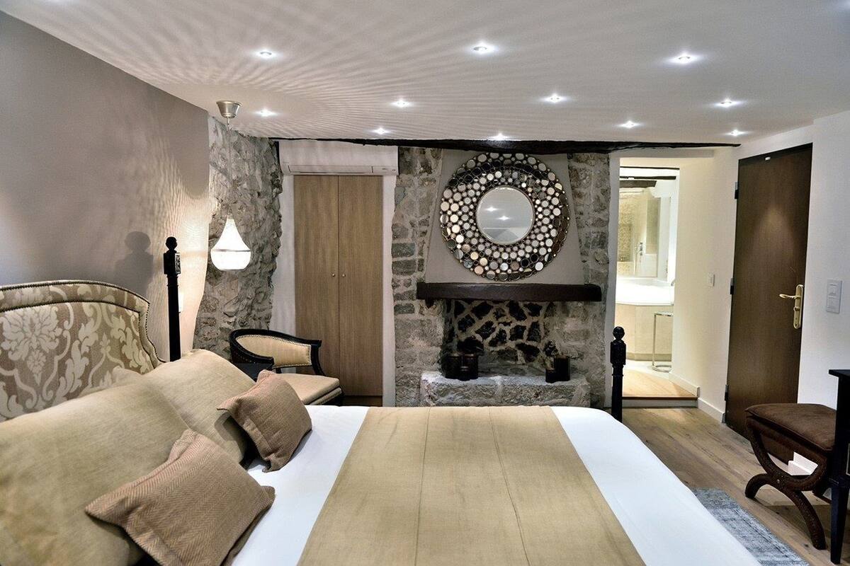 A bedroom with a bed, a stone fireplace, a mirror, and a door leading to a bathroom.