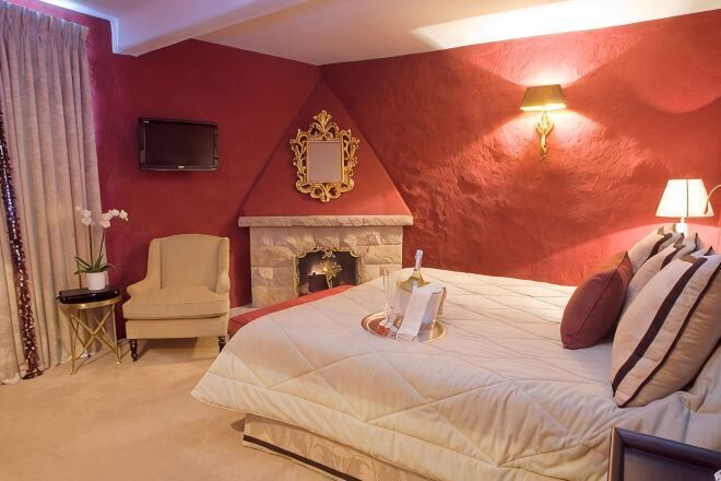 A bedroom with a bed, a chair, a fireplace, and a television.