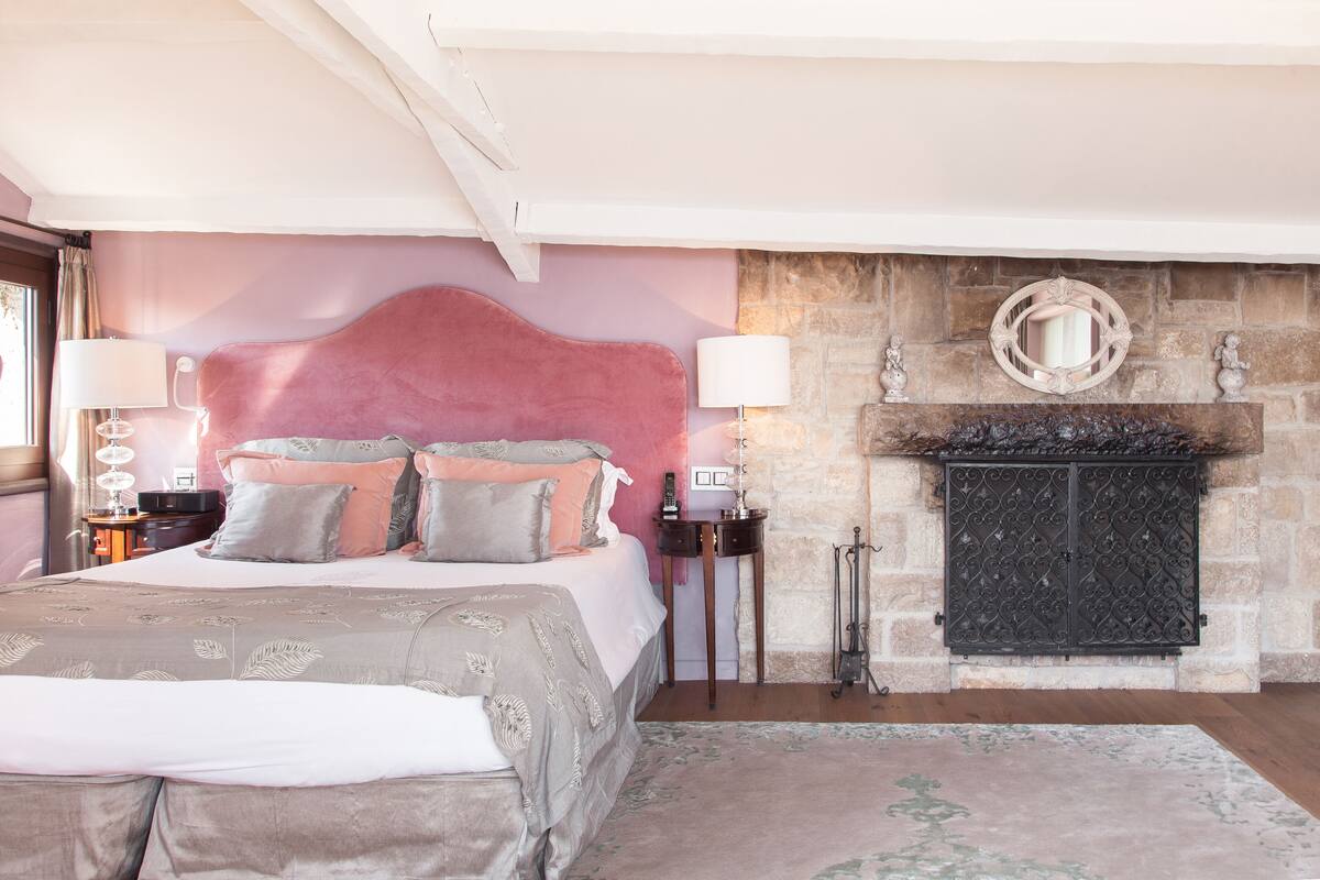 A bedroom with a large bed, a stone fireplace, and a mirror above it.