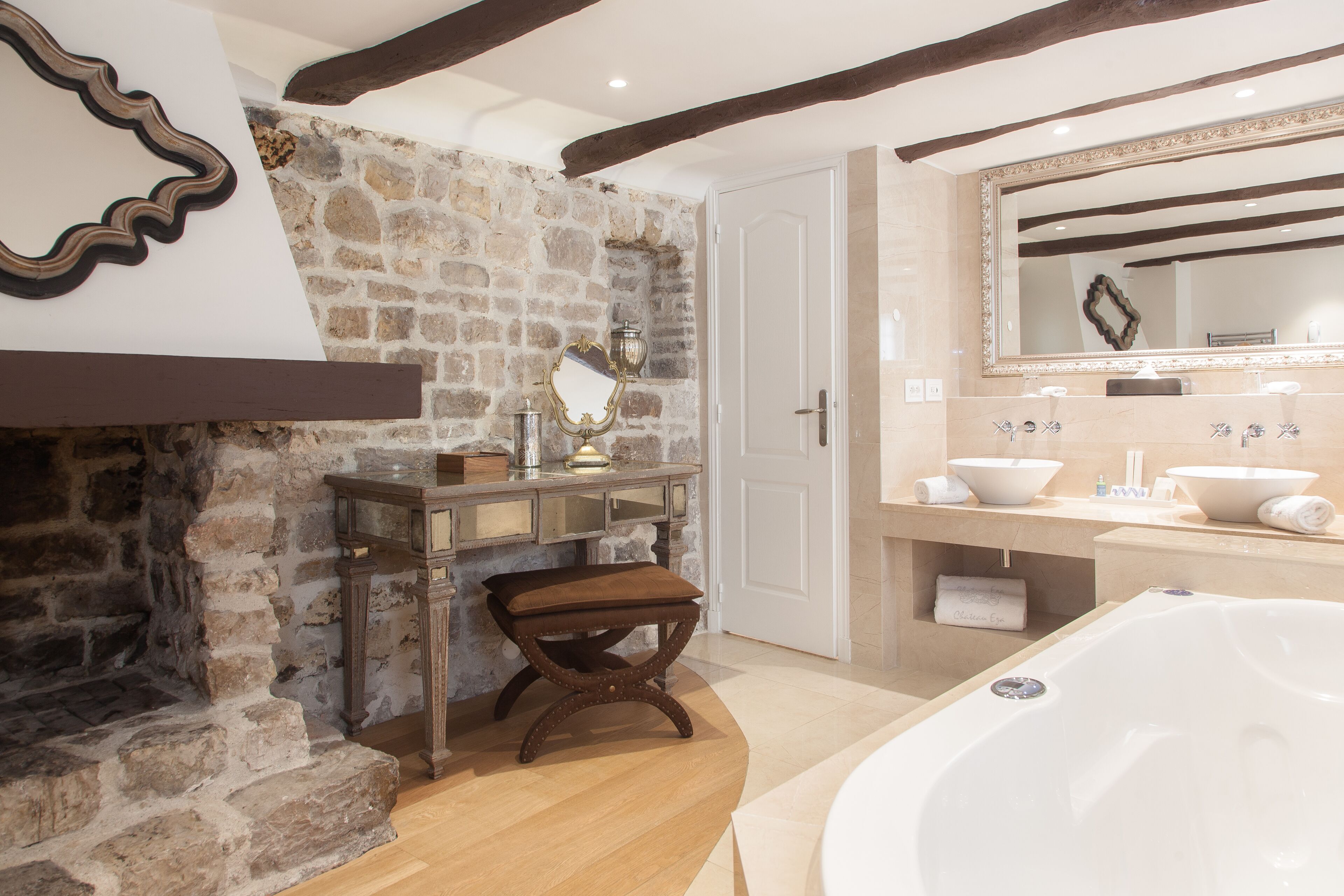 Un baño con pared de piedra, banco de madera, bañera y un espejo grande.