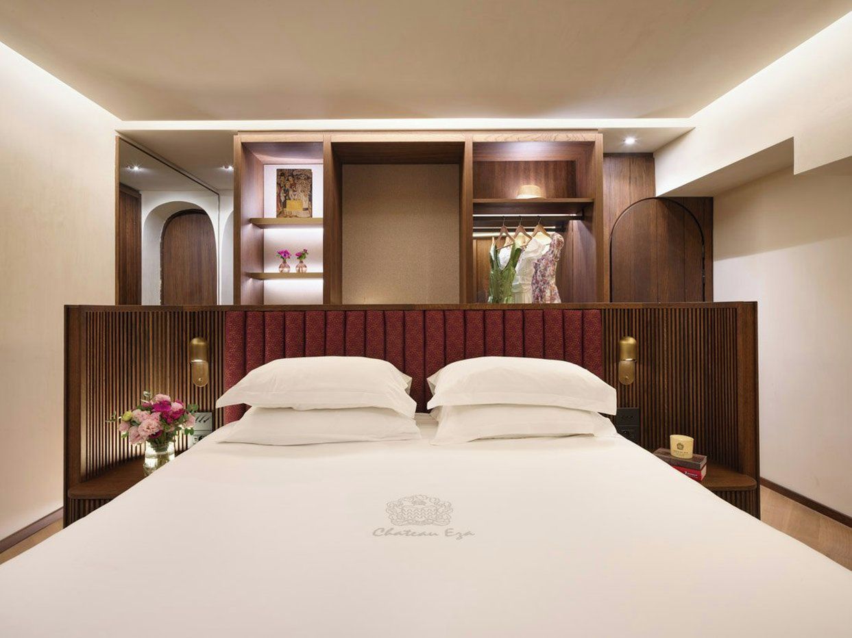Une chambre d’hôtel avec un grand lit, une tête de lit en bois, une table de chevet et une petite table sur laquelle est posé un vase de fleurs.