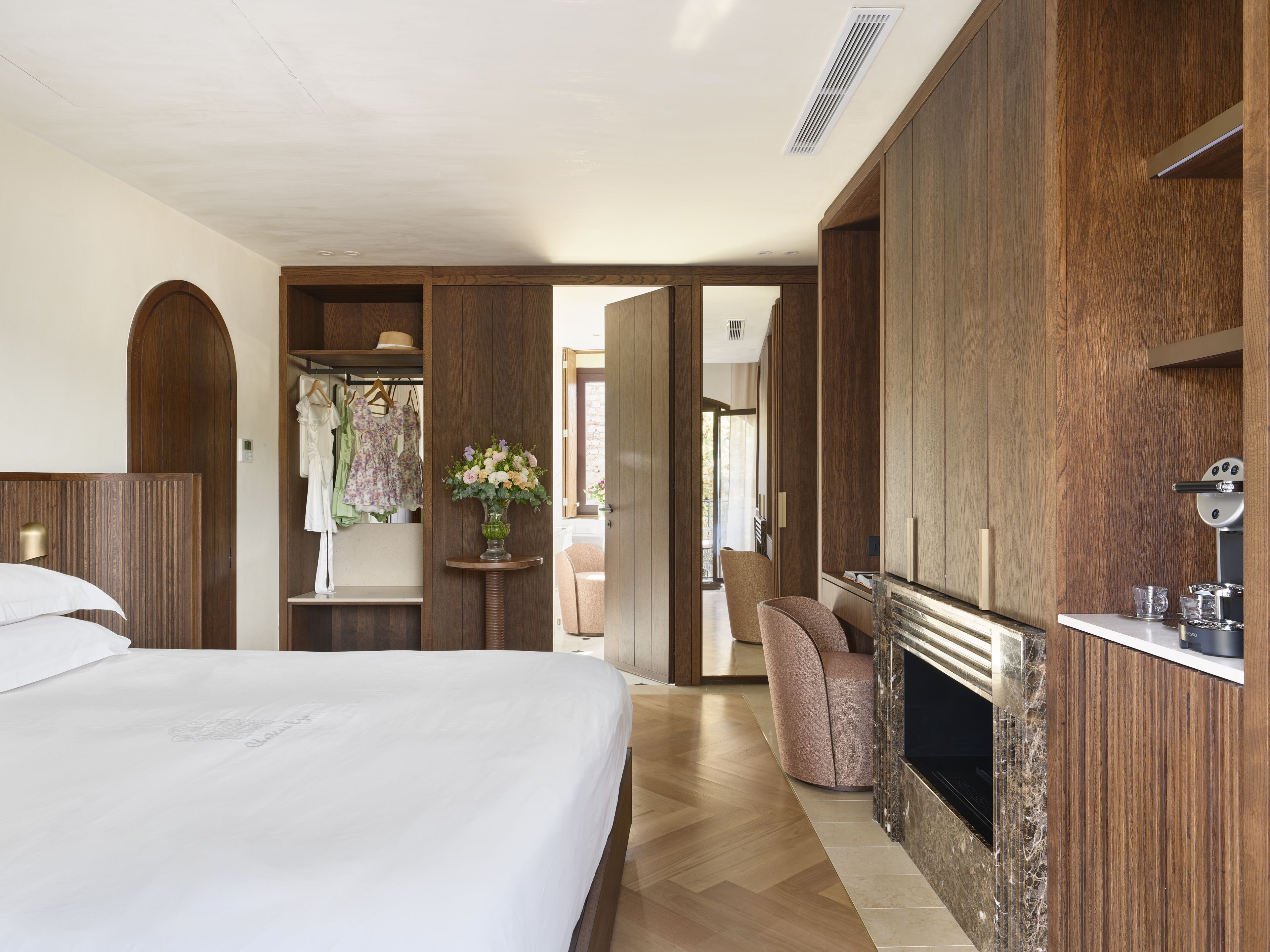 Una habitación de hotel moderna con una cama grande, una chimenea, un armario de madera y una zona de estar.