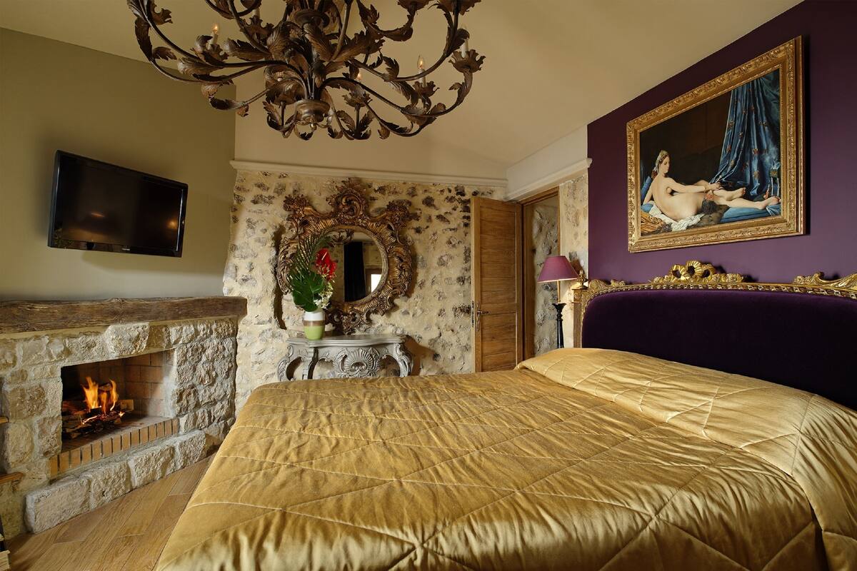 A bedroom with a large bed, a fireplace, a television, and a painting on the wall.