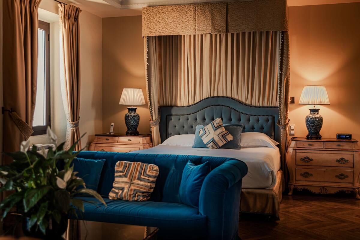 A hotel room with a large bed, a blue sofa, two bedside tables with lamps, and a window with curtains.