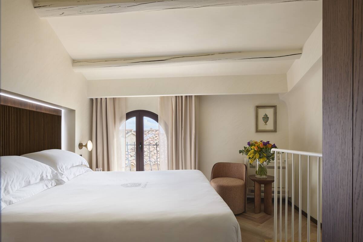 A hotel room with a large bed, a small table with a vase of flowers, a chair, and a view of the outside.