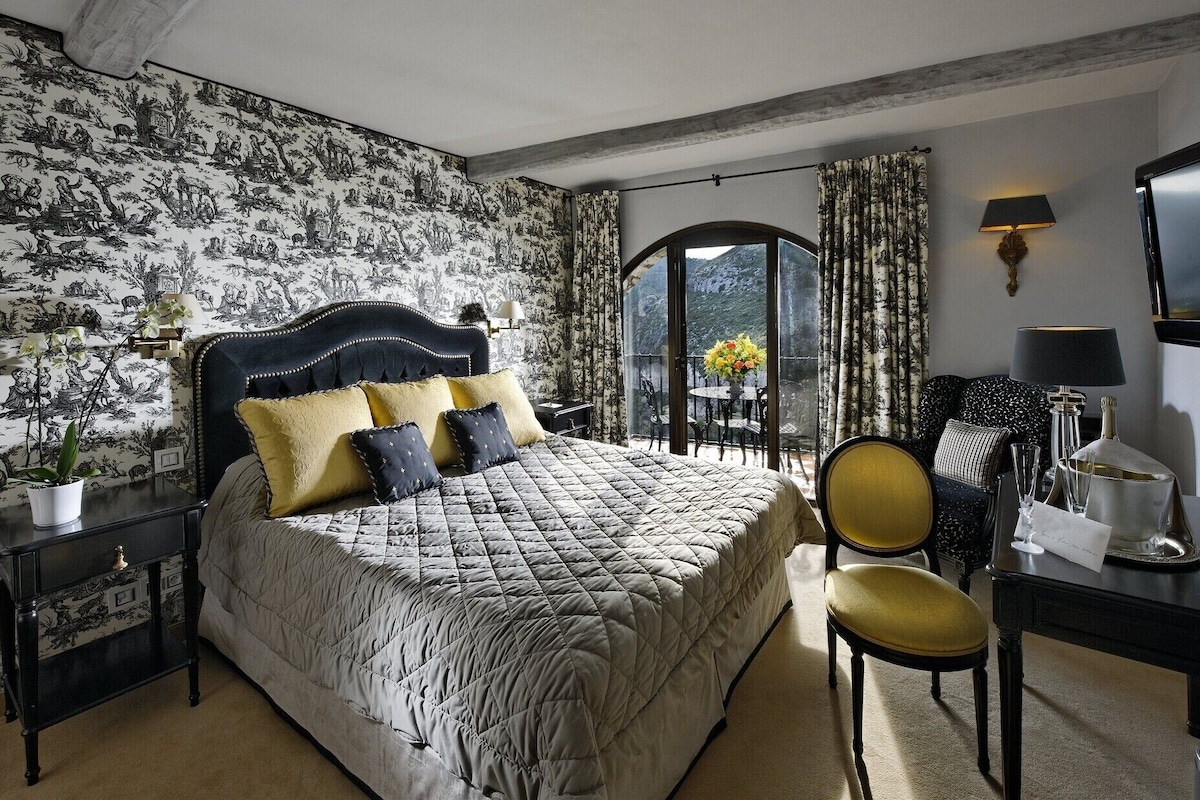 A bedroom with a large bed, a desk, a chair, and a view of the outdoors.