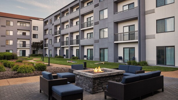 A modern outdoor seating area with a fire pit, surrounded by wicker furniture and a landscaped garden.
