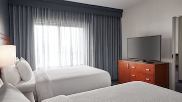 Une chambre d’hôtel avec deux lits, un téléviseur posé sur un meuble en bois et une grande fenêtre avec des rideaux.